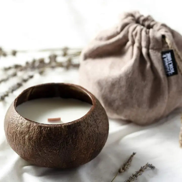 Candle in a coconut shell with a drawstring bag and lavender on a light background