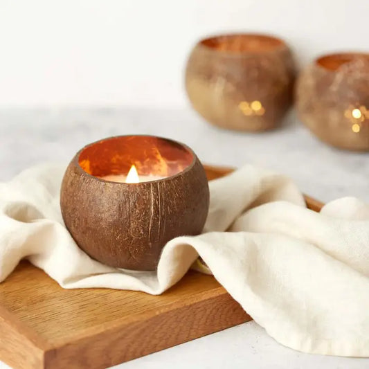 Coconut shell candle holders with lit candles on a wooden surface and white cloth