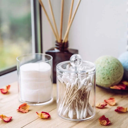 Clear glass jars with cotton balls, cotton swabs, and bath bombs on a wooden surface.