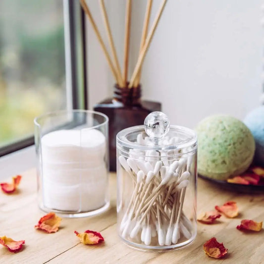 Clear glass jars with cotton balls, cotton swabs, and bath bombs on a wooden surface.