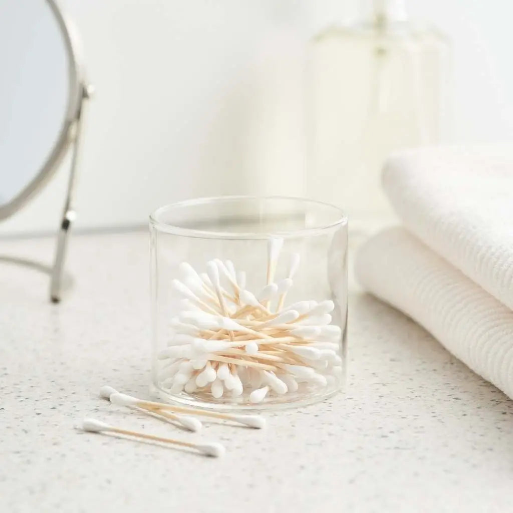 Clear glass container with cotton swabs on a light surface
