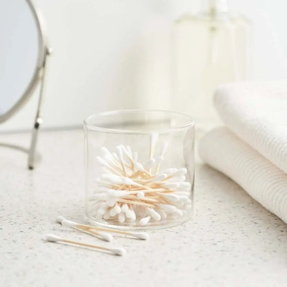 Clear glass container with cotton swabs on a light surface