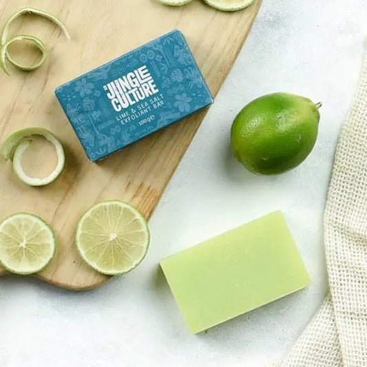 Green soap bar next to a box labeled 'Jingle Culture' on a wooden board with limes.