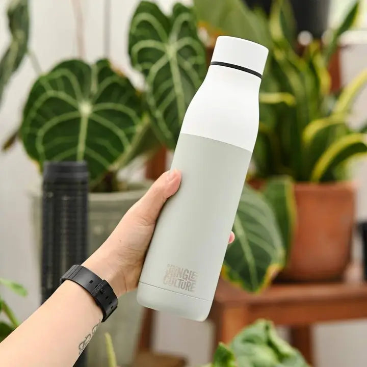 Person holding a white water bottle with plants in the background